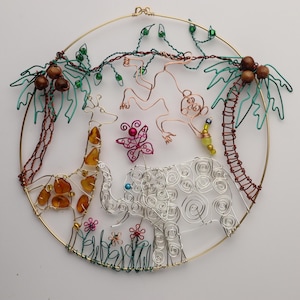 Puede incluir: Escultura de alambre de una jirafa, un elefante, un mono y una mariposa en un marco redondo de color dorado. La escultura está hecha de cobre, plata y cuentas de color ámbar. El fondo es blanco.