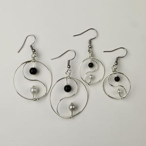 May include: Three pairs of silver earrings with a yin yang design. Each earring features a black and white bead in the center of the yin yang symbol.