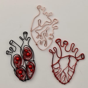 May include: Three wire heart sculptures. One is black with red beads, one is red, and one is copper.