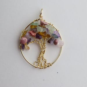 Op de afbeelding: Een gouden draadgewikkelde levensboomhanger met een verscheidenheid aan gekleurde edelstenen, waaronder roze, paars, groen en geel.