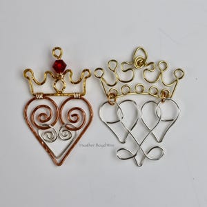 Puede incluir: Dos adornos de corona de alambre. Uno es dorado y cobrizo con un diseño en forma de corazón y una gema roja. El otro es dorado y plateado con un diseño en forma de corazón. Adornos hechos a mano.