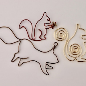 May include: Three wire sculptures of squirrels. One is red, one is gold, and one is silver. The gold squirrel has a spiral tail.
