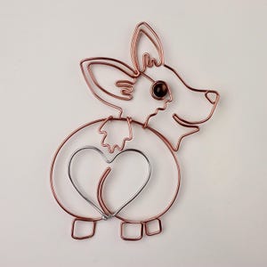 May include: A wire sculpture of a dog with a heart-shaped tail. The dog is made of copper wire and has a brown eye. The sculpture is on a white background.