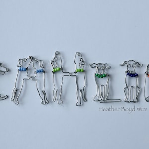 Könnte beinhalten: Der Name "CALLIE" wird mit Drahtskulpturen von Hunden buchstabiert. Jeder Hund trägt ein farbiges Perlenhalsband. Der Text "Heather Boyd Wire" befindet sich am unteren Rand des Bildes.