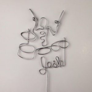 Peut inclure: Une sculpture en fil d'argent d'un batteur jouant de la batterie avec le mot "Josh" écrit en dessous.