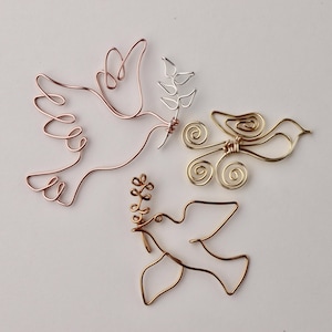 May include: Three wire sculptures of doves, each with a different colour of wire. One dove is made of rose gold wire, one is made of gold wire, and one is made of silver wire. Each dove has a small branch of leaves in its beak.