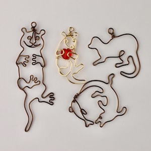 May include: Four wire sculptures of animals, each with a loop at the top for hanging. The sculptures are made of copper wire and are in the shapes of a cat, a dog, a fish, and a bird. The bird is holding a red glass bead in its claws.