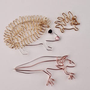 May include: Three wire sculptures of animals: a gold hedgehog, a silver hedgehog, and a copper lizard.