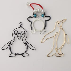 May include: Three wire penguin ornaments. One is black with blue eyes and a red and white hat with white beads. One is gold and one is black.