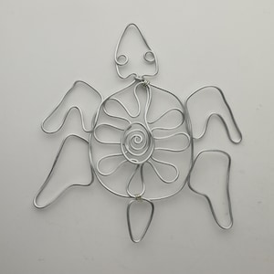 Op de afbeelding: Een zilveren draadbeeld van een schildpad met een bloemendesign op zijn schild. De schildpad heeft een eenvoudig, afgerond hoofd en vier poten.