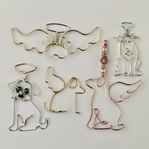 Puede incluir: Seis adornos de perro de alambre, algunos con alas de ángel, otros con halos. Los adornos están hechos de alambre de plata, oro y cobre. Un adorno tiene una cadena de cuentas moradas y blancas.