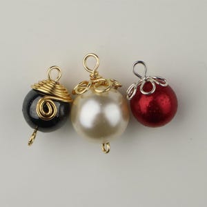 Può includere: Tre piccoli addobbi natalizi con anelli di filo. Gli addobbi sono neri, bianchi e rossi. L'addobbo nero ha un filo dorato avvolto attorno. L'addobbo bianco ha un anello di filo dorato nella parte superiore. L'addobbo rosso ha un anello di filo argentato nella parte superiore.