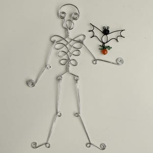 May include: A silver wire skeleton holding a black wire bat with an orange bead pumpkin.