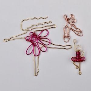 May include: Three wire sculptures of dancers. The largest dancer is gold with a pink wire skirt. The other two dancers are smaller and are gold and copper with pink wire skirts.
