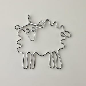 May include: A silver wire sculpture of a sheep. The sheep has a curly tail and a loop at the top for hanging.