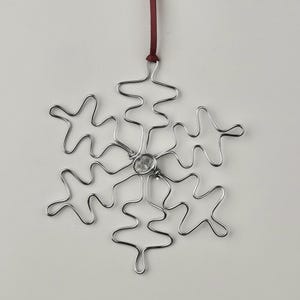 May include: A silver wire snowflake ornament with a clear crystal in the centre. The snowflake is hanging from a red ribbon.