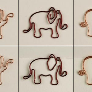 K&ouml;nnte beinhalten: Sechs Drahtskulpturen von Elefanten, drei in Kupfer und drei in Rot, sind in einem Gittermuster angeordnet. Jeder Elefant besteht aus einem einzigen Drahtst&uuml;ck und hat einen eingerollten R&uuml;ssel.