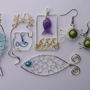 May include: A collection of handmade wire jewelry pieces in the shape of fish and aquatic themes. Includes earrings with green beads, pendants with blue and purple stones, and a fishbowl design. The wire is silver and gold colored.