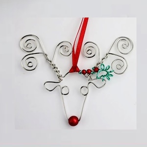 May include: A silver wire reindeer ornament with red beads and a green wire holly sprig. The ornament has a red ribbon for hanging.