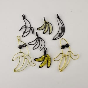 May include: A set of six wire banana charms, some with black wire and some with gold wire. Some of the bananas have black beads for eyes and a gold wire for sunglasses. Some of the bananas have yellow beads for the banana peel.