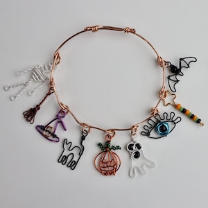 Op de afbeelding: Een koperdraadarmband met Halloween-charms. Charms zijn onder meer een skelet, heksenhoed, zwarte kat, pompoen, spook, oog, vleermuis en ster. Een feestelijk accessoire voor het griezelige seizoen.