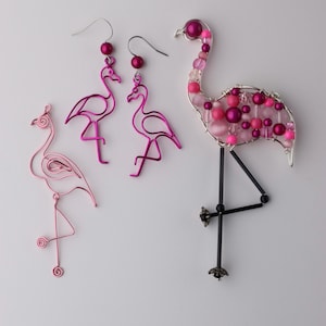 May include: Three pink flamingo wire sculptures. Two are earrings and one is a larger, beaded sculpture.