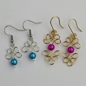 May include: Two pairs of earrings with a knotted design. One pair is silver with a turquoise bead and the other is gold with a pink bead.