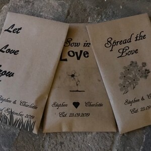 May include: Three brown paper seed packets with black text and illustrations. The packets read "Let Love Grow", "Sow in Love", and "Spread the Love". Each packet includes the names "Stephen & Charlotte" and the date "23.09.2019".