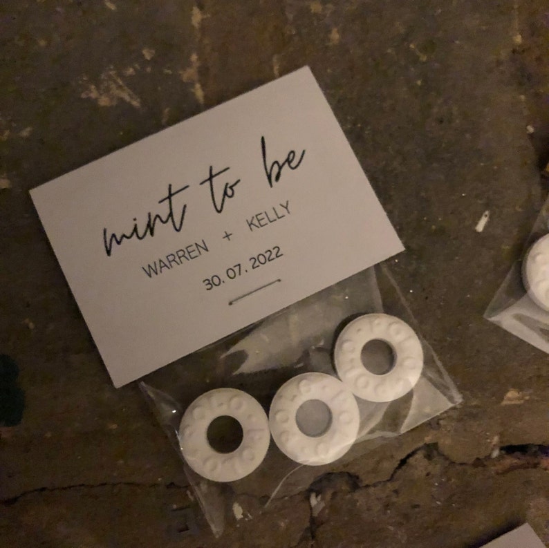 May include: A white card with black text that reads "mint to be" with the names "Warren + Kelly" and the date "30.07.2022". The card is in a clear plastic bag with three white round mints.