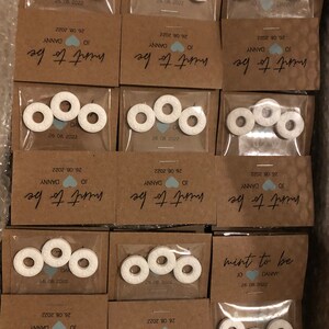 May include: A set of small, white, round mints with a hole in the center, packaged in clear plastic bags with brown paper cards. The cards have the text "mint to be" with the date and names "JO & DANNY" printed on them.