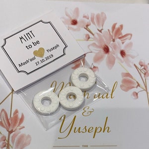 May include: A white card with gold lettering that reads "Mint to be Mash'aal & Yuseph 27.10.2019". There are three white round mints in a clear plastic bag.