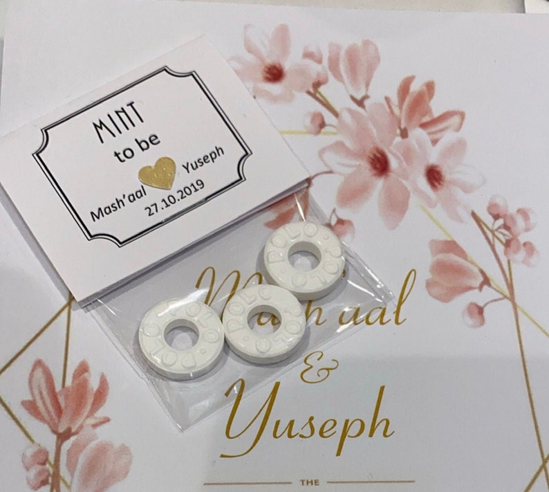 May include: A white card with gold lettering that reads "Mint to be Mash'aal & Yuseph 27.10.2019". There are three white round mints in a clear plastic bag.