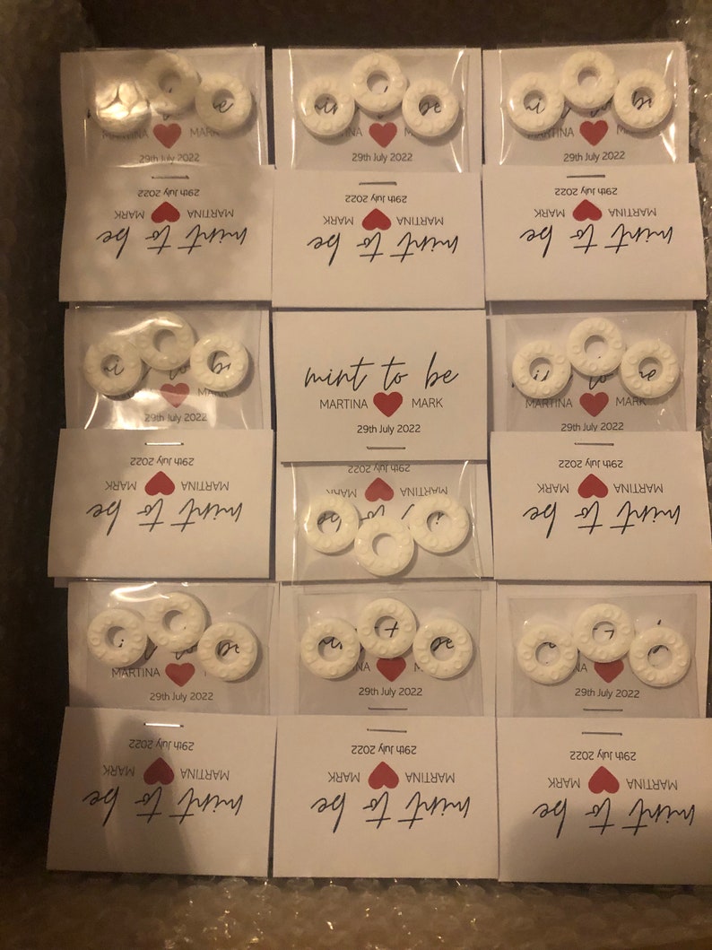 May include: Mint to be wedding favors with white round mints and a white card with the text "mint to be" in black cursive writing, "MARTINA" and "MARK" in black text, and "29th July 2022" in black text.