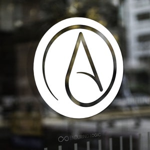 May include: White logo on a glass door. The logo is a stylized letter "A" inside a circle. The text "Enduring Logic" is below the logo. The background is blurred, showing a city scene.