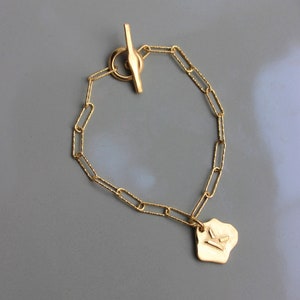 Peut inclure: Un bracelet en or avec un fermoir à glissière et un petit charme en or texturé. Le charme a un design géométrique.