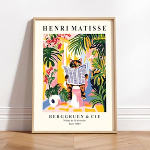 Op de afbeelding: Een ingelijste kunstprint met een kat die een krant leest op een toilet, tegen een kleurrijke achtergrond van tropische planten. De print bevat de tekst "HENRI MATISSE" en "BERGGRUEN & CIE" bovenaan en onderaan.