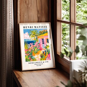 May include: A vintage poster featuring a colorful illustration of a pink house with a palm tree and flowers. The poster is titled "Henri Matisse" and includes the text "Berggruen & Cie 70 Rue de l'Universit&eacute; Paris 75007".