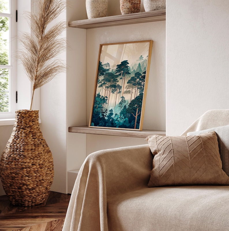 May include: A framed print of a forest scene with tall, dark green trees and a light blue sky. The print is hanging on a white wall above a beige couch with a brown throw pillow.