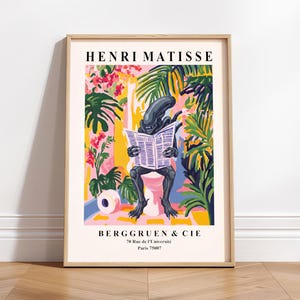 Op de afbeelding: Een ingelijste kunstprint met een alien die een krant leest op een toilet, tegen een kleurrijke achtergrond van tropische planten en bloemen. De print bevat de tekst "HENRI MATISSE" en "BERGGRUEN & CIE", met het adres in Parijs.