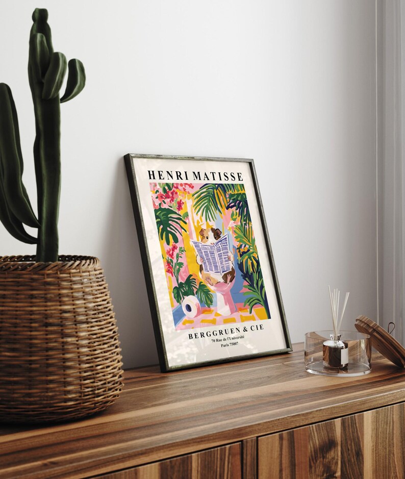 May include: Framed Henri Matisse art print featuring a colorful illustration of a person reading a newspaper amidst tropical foliage. The print includes the text "BERGGRUEN & CIE" and is displayed on a wooden surface.