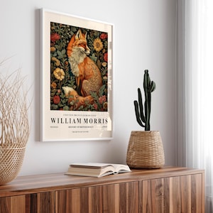 May include: A framed poster with a vintage aesthetic featuring a red fox surrounded by flowers. The poster is titled "COTTON PRINTS EXHIBITION WILLIAM MORRIS TEXTILES HISTORY OF BRITISH DESIGN THE ART OF SIX CENTURIES".