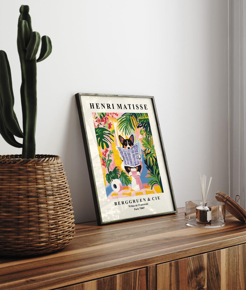 Puede incluir: Impresi&oacute;n art&iacute;stica enmarcada que presenta una ilustraci&oacute;n caprichosa de un corgi leyendo un peri&oacute;dico, sobre un vibrante fondo de follaje tropical. La impresi&oacute;n est&aacute; etiquetada como "HENRI MATISSE" y "BERGGRUEN & CIE". La obra de arte se exhibe sobre una superficie de madera.