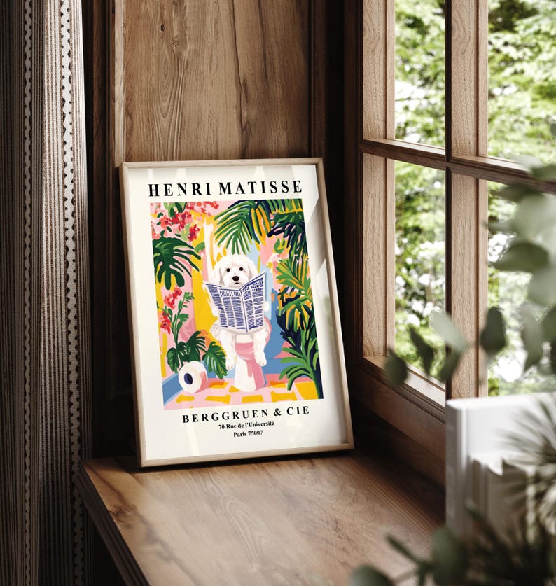 May include: A framed art print displaying a white dog reading a newspaper, set against a vibrant background of tropical plants and flowers. The print is labelled "HENRI MATISSE" and "BERGGRUEN & CIE" in a wooden frame.