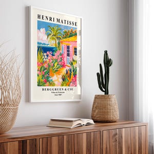 May include: A framed poster with a colorful painting of a pink house with a garden and a blue ocean in the background. The poster is titled "Henri Matisse" and has the text "Berggruen & Cie" at the bottom.
