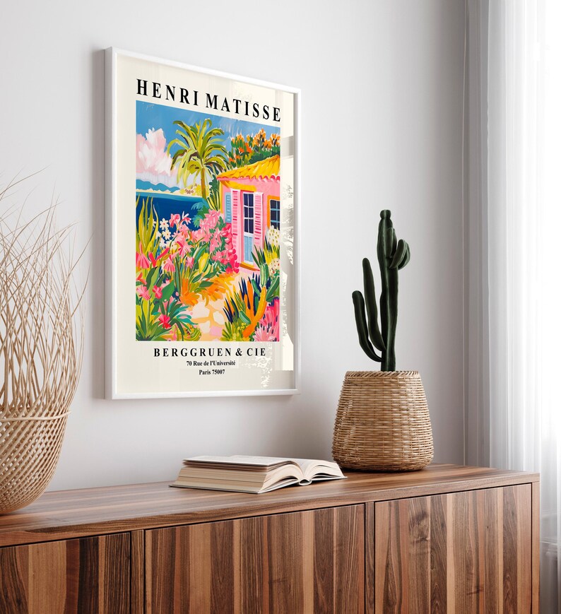 May include: A framed poster with a colorful painting of a pink house with a garden and a blue ocean in the background. The poster is titled "Henri Matisse" and has the text "Berggruen & Cie" at the bottom.