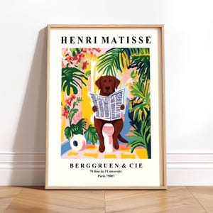 May include: A framed art print depicting a brown dog on a toilet, reading a newspaper, in a colourful, Matisse-inspired style. The print includes tropical plants and the text "HENRI MATISSE" at the top, with a beige border.