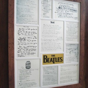 Puede incluir: Una colecci&oacute;n enmarcada de letras escritas a mano de los Beatles, incluyendo "Hey Jude", "Get Back", "She's Leaving Home" y "Taxman". Las letras se muestran en un marco blanco con un borde dorado y un logotipo dorado de "The Beatles".