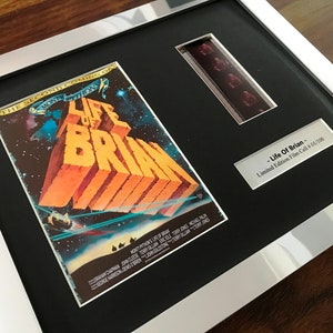 May include: A framed film cell from the movie "Life of Brian" by Monty Python. The cell is numbered 01/100 and is displayed with a poster featuring the film's title in large, yellow letters against a dark, starry background.