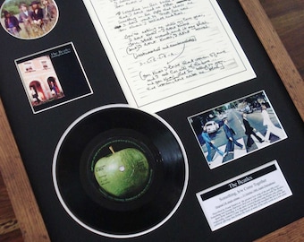 May include: A framed display of The Beatles memorabilia, including a handwritten lyric sheet for the song "Something", a 45 rpm record with a green apple on the label, a photo of the band crossing Abbey Road, and a photo of the band members.