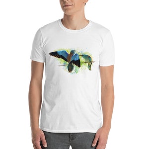 May include: A white t-shirt with a watercolor design of two blue-green birds perched on a branch. The birds are facing each other and have brown and blue feathers.